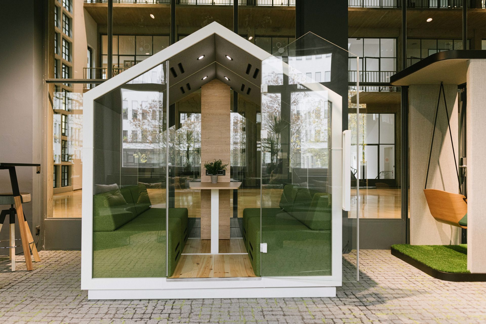 treehouse TH 4 Akustikkabine: Büro-Telefonzelle mit Glaswänden, grünen Sofas und Holztisch für vier Personen.